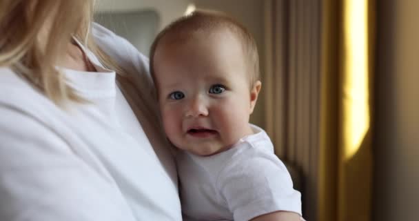 Giovane madre caucasica e la sua bambina abbracciano e giocano a casa in camera da letto. Bambino di sette mesi che trascorre del tempo con le braccia della mamma a casa vicino alla finestra, al rallentatore. — Video Stock