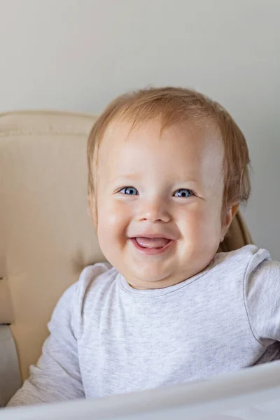 Menina bonito caucasiano bebê dez meses de idade sentado em cadeira de bebê e sorrindo em fundo bege. Retrato de close-up de bebê feliz com cabelo loiro e olhos azuis — Fotografia de Stock