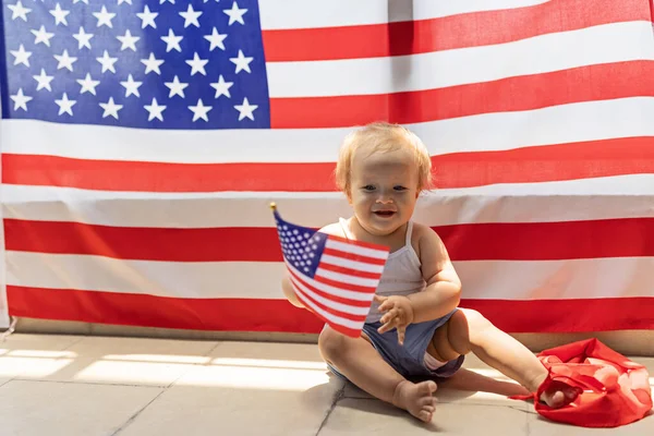 Patriotic holiday. Cute caucasian baby ten-eleven months old with blonde hair and blue eyes with American flag at home. USA celebrate independence day 4th of July. — Stock Photo, Image