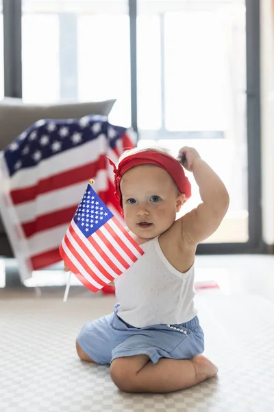 Patriotic holiday. Cute caucasian baby ten-eleven months old with blonde hair and blue eyes with American flag at home. USA celebrate independence day 4th of July. — Stock Photo, Image