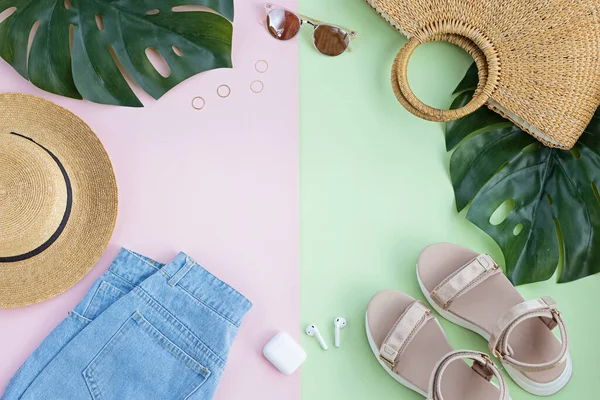 Composición de verano con atuendo de moda femenina. Hojas de monstera, sombrero de paja, bolsa de bambú, zapatos, auriculares inalámbricos sobre fondo pastel. plano, vista superior, arriba, maqueta, plantilla, espacio para copiar —  Fotos de Stock