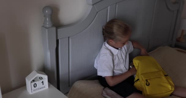 Schattige blanke basisschool meisje dragen uniform en verpakking rugzak thuis op bed, kind voor te bereiden voor de eerste dag op school na einde Coronavirus covid-19 quarantaine. Langzame beweging — Stockvideo