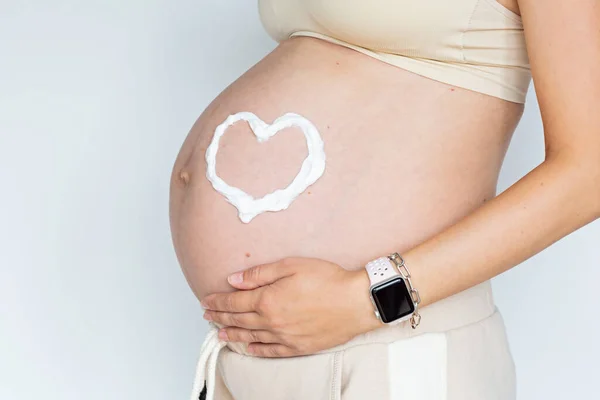 Fotografía de cerca de la joven mujer tocando las manos de su gran vientre desnudo Aislado sobre fondo blanco con espacio de copia. Cuidado de la piel con crema hidratante contra las estrías. Embarazo emocional amoroso — Foto de Stock