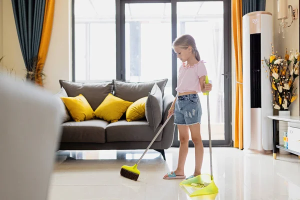 Menina loira caucasiana com cabelo loiro sete anos de idade chão de limpeza na sala de estar. Interior de casa moderno, vida doméstica. — Fotografia de Stock