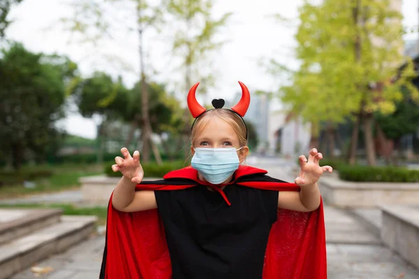 Portrait of cute Little Girl in costume of evil at home. Happy Halloween during coronavirus covid-19 pandemic quarantine concept. Kid wearing medical mask — Stock Photo, Image