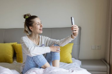 Kafkasyalı genç bir kadın cep telefonu ve kablosuz kulaklık kullanıyor, dinleniyor, yatakta oturuyor ve podcast ya da kulüp binasını dinliyor - sadece sesli sosyal medya uygulaması, sesli sohbet