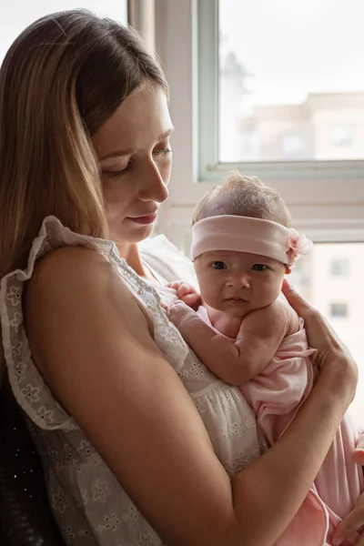 Portret van jonge blanke moeder houdt knuffel kleine pasgeboren baby twee weken oud thuis. gelukkig mam omarmt kleine zuigeling kind, shows liefde en zorg, kinderopvang concept — Stockfoto