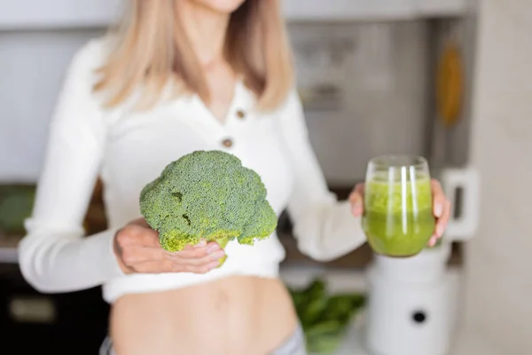 Young caucasian woman with blonde hair making detox cocktail in blender with fresh green vegetables on kitchen at home — Stock Photo, Image