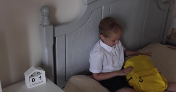 Bonito caucasiano escola primária menina vestindo uniforme e mochila de embalagem em casa na cama, criança se preparando para o primeiro dia na escola após o fim Coronavirus covid-19 quarentena. Movimento lento — Vídeo de Stock