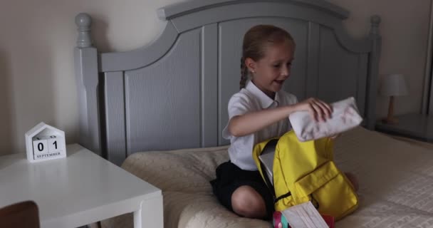 Mignonne fille de l'école primaire caucasienne portant uniforme et sac à dos d'emballage à la maison sur le lit, enfant se préparant pour le premier jour à l'école après la fin de la quarantaine Coronavirus covid-19. Mouvement lent — Video