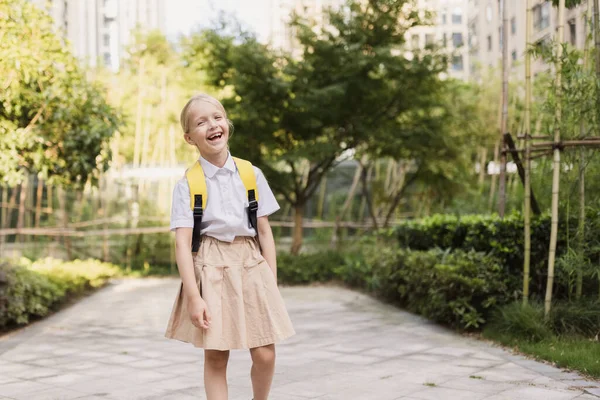 Schoolmeisje terug naar school na de zomervakantie. Pupil in uniform glimlachen vroeg in de ochtend buiten. — Stockfoto