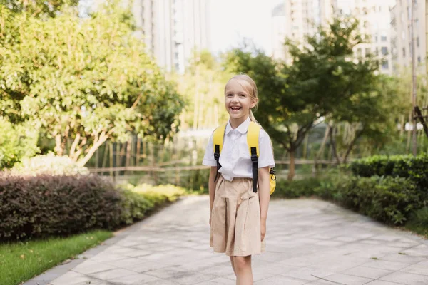 Schoolmeisje terug naar school na de zomervakantie. Pupil in uniform glimlachen vroeg in de ochtend buiten. — Stockfoto