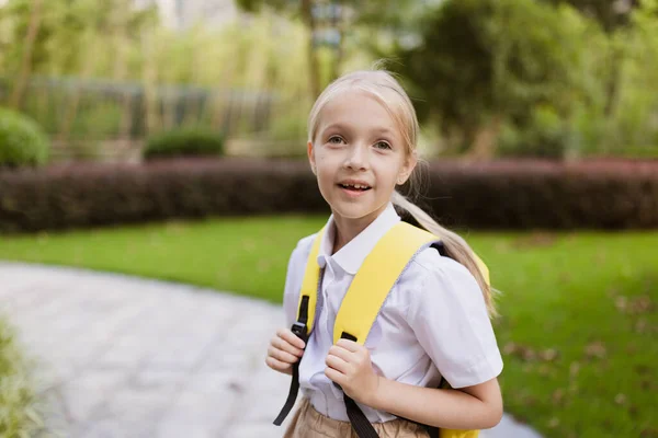 Skolflicka tillbaka till skolan efter sommarlovet. Pupil i uniform ler tidigt på morgonen utomhus. — Stockfoto