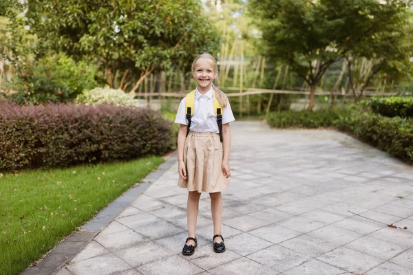 Schoolmeisje terug naar school na de zomervakantie. Pupil in uniform glimlachen vroeg in de ochtend buiten. — Stockfoto