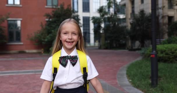 Happy little caucasian blonde girl seven years old in uniform with yellow backpack going back to school after summer vacations or Coronavirus covid-19 quarantine. 4k slow motion — Stock Video