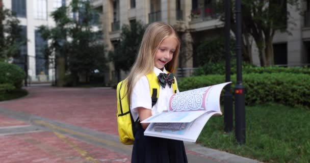 Šťastná malá kavkazská blondýnka, sedmiletá v uniformě se žlutým batohem, čtečka u školy po letních prázdninách nebo v karanténě Coronavirus covid-19. 4k zpomalený pohyb — Stock video