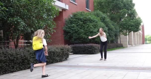 Šťastná malá bílá blondýnka v uniformě se žlutým batohem běžící k matce po vyučování ve škole. 4k zpomalený pohyb — Stock video