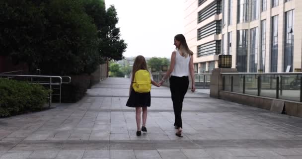 Feliz niña rubia caucásica de siete años de edad en uniforme con mochila amarilla que regresa a la escuela después de las vacaciones de verano o Coronavirus covid-19 cuarentena con madre joven. 4k cámara lenta — Vídeos de Stock