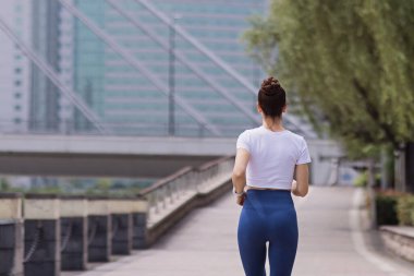 Yaz parkında asfalt yolda koşan genç esmer kadın. Aktif beyaz kadın sporcu sabah sporu yapıyor. Spor giyim sektöründe sportif kişi dışarıda egzersiz yapıyor. Giyinik taytlar ve spor bluzlar.