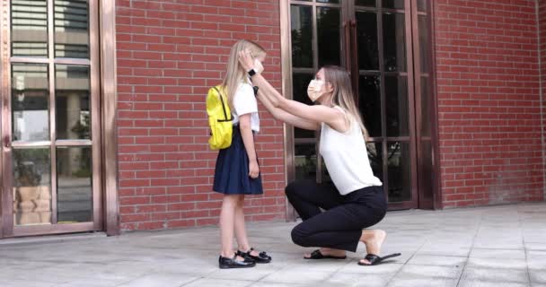 Feliz niña rubia caucásica de siete años de edad en uniforme con mochila amarilla que regresa a la escuela después de las vacaciones de verano o Coronavirus covid-19 cuarentena con madre joven. 4k cámara lenta — Vídeo de stock