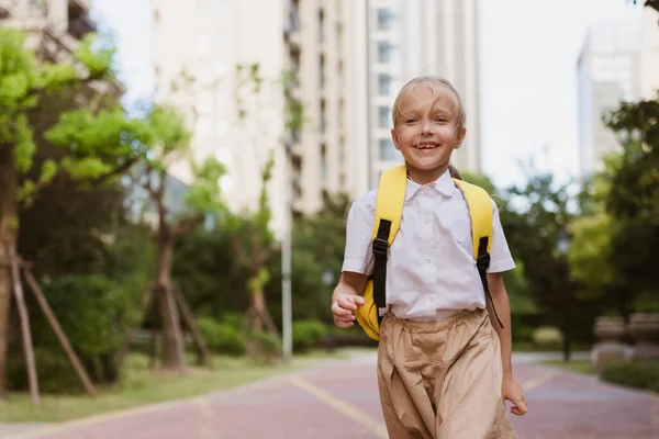 Skolflicka tillbaka till skolan efter sommarlovet. Barn i uniform ler tidigt på morgonen utomhus. — Stockfoto