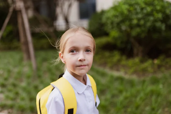 Uczennica wraca do szkoły po wakacjach. Dziecko w mundurze uśmiecha się wcześnie rano na świeżym powietrzu. — Zdjęcie stockowe
