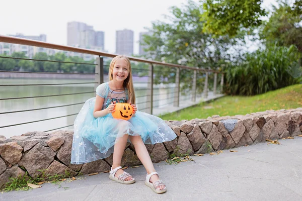 Lilla blonda flicka i prinsessdräkt med pumpa lykta i parken. Glad Halloween koncept — Stockfoto