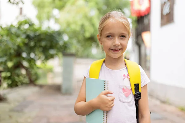 Školačka se po letních prázdninách vrací do školy. Šťastné dítě s úsměvem brzy ráno venku. — Stock fotografie