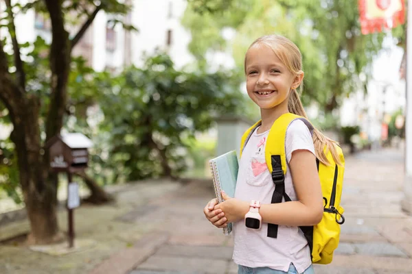 Skolflicka tillbaka till skolan efter sommarlovet. Glada barn ler tidigt på morgonen utomhus. — Stockfoto