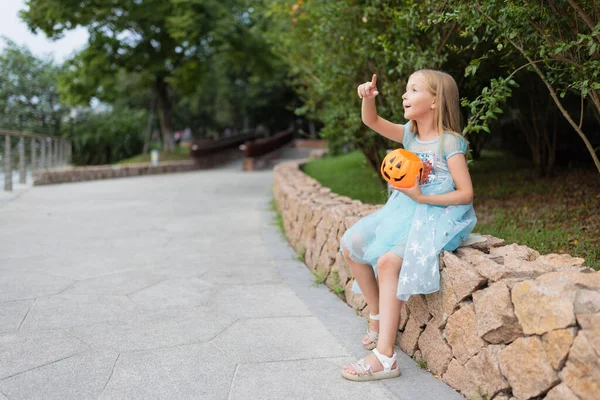 Mała blondynka w kostiumie księżniczki z dyniową latarnią w parku. Szczęśliwego Halloween koncepcja — Zdjęcie stockowe