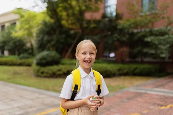 Schoolmeisje terug naar school na de zomervakantie. Kind in uniform staat vroeg in de ochtend buiten. — Stockfoto