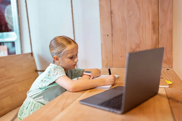 happy caucasian kid has online lesson on laptop during coronavirus covid-19 pandemic and lockdown