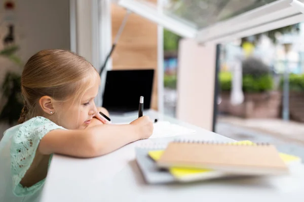 happy caucasian kid has online lesson on laptop during coronavirus covid-19 pandemic and lockdown