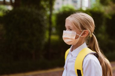 Okula giderken koronavirüs salgını sırasında koruyucu yüz maskesi takan okul çocuğu