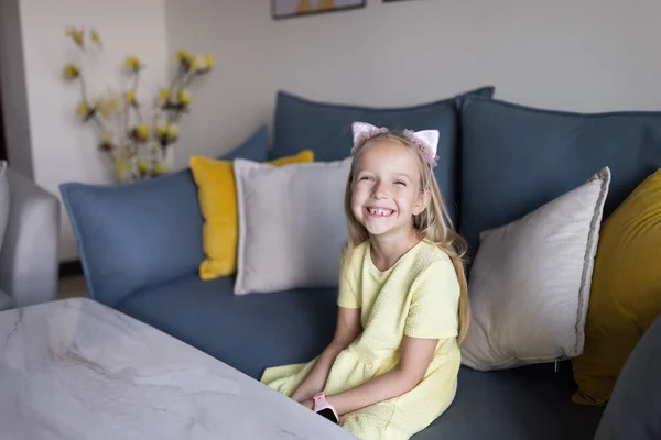Carino piccola ragazza caucasica di sette anni con i capelli biondi seduti sul divano a casa in appartamento — Foto Stock