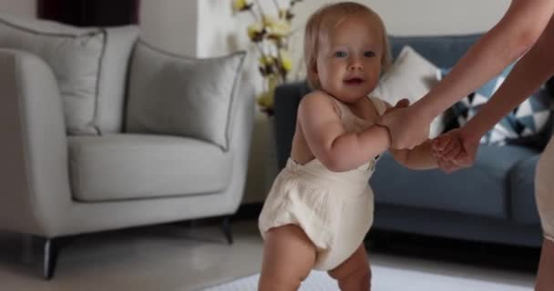 Carino caucasico neonata con i capelli biondi e occhi azzurri un anno vecchio apprendimento a piedi. Bambino che fa i primi passi a casa. Sorella maggiore che sostiene il bambino che impara ad andare. Felice nuovo concetto di vita. Poco. — Video Stock