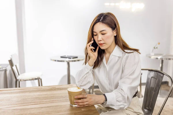 Smiling Asian Woman Talking On Cellphone In Cafe, Managing Her Business Schedule, Planning Meetings, Talking With Client or friends, Sitting At Table In modern Cafeteria