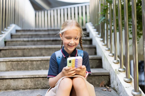 Lilla kaukasiska flicka leker med mobiltelefon i ny pop det leksak fall. Utveckling av finmotorik, Push bubbla fidget sensorisk leksak - tvättbar och återanvändbar kisel stress lättnad leksak. Anti — Stockfoto