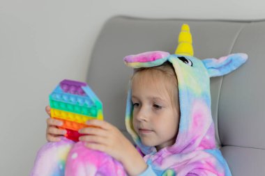 Küçük beyaz kız yeni moda pop it oyuncağıyla oynuyor. Kaliteli motor becerilerin geliştirilmesi, kabarcık duyusal oyuncak itmek - yıkanabilir ve yeniden kullanılabilir silikon stres giderici oyuncak. Stres önleyici oyuncak