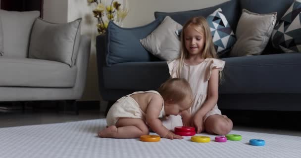Zwei niedliche kleine kaukasische Kinder Geschwister spielen zusammen mit Holzspielzeug auf dem Boden zu Hause. Entwicklungskonzept für Kinder. Säugling Mädchen mit blonden Haaren spielt mit der älteren Schwester. Zeitlupe 4k — Stockvideo