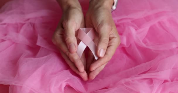 Nastro rosa di consapevolezza del cancro al seno in mani su sfondo rosa. Rallentatore. — Video Stock