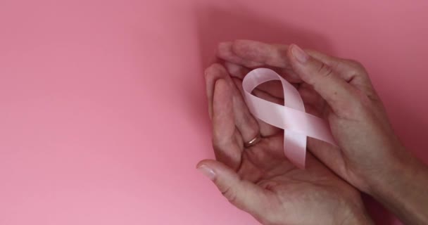 Rosa bröstcancer medvetenhet band i händerna på rosa bakgrund. Långsamma rörelser. — Stockvideo