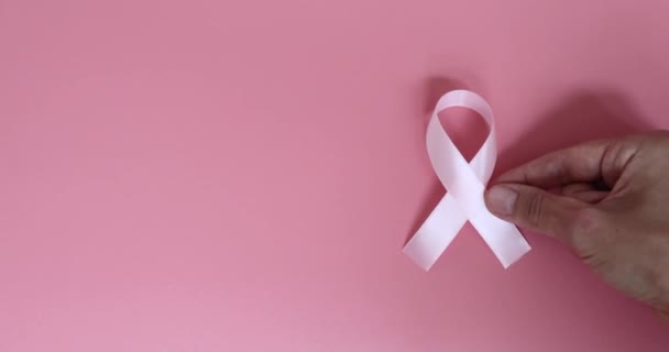 Pinkfarbenes Brustkrebs-Bewusstseinsband und Hand auf rosa Hintergrund. Zeitlupe. — Stockvideo
