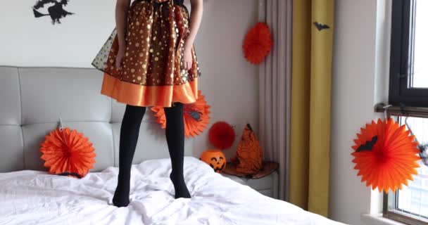 Cute dziewczynka kaukaska z blond włosami siedem lat w strój czarownicy i kapelusz zabawy i świętowania Halloween w domu podczas pandemii i kwarantanny Coronavirus covid-19. Zwolniony ruch — Wideo stockowe