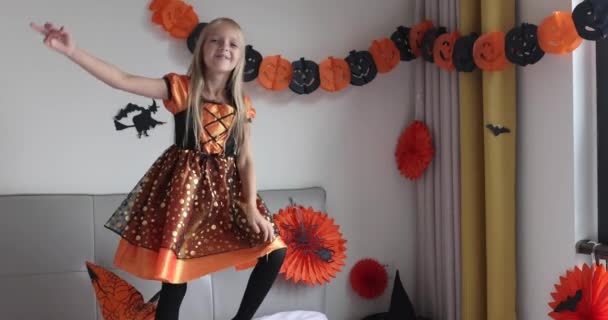 Söt vit liten flicka med blont hår sju år gammal i häxa klänning och hatt har roligt och firar Halloween hemma under Coronavirus covid-19 pandemi och karantän. Långsamma rörelser — Stockvideo