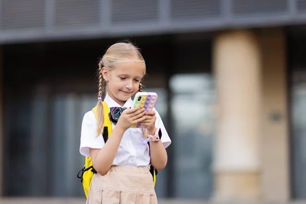 Lilla kaukasiska flicka leker med mobiltelefon i ny pop det leksak fall. Utveckling av finmotorik, Push bubbla fidget sensorisk leksak - tvättbar och återanvändbar kisel stress lättnad leksak. Anti — Stockfoto