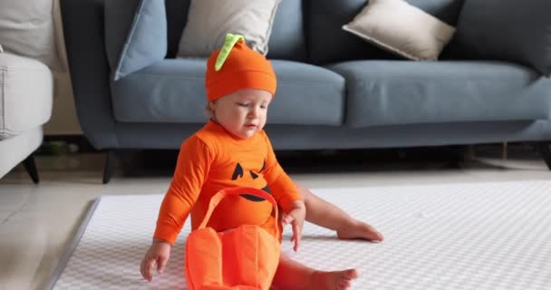 Bébé fille blanche mignonne d'un an en vêtements orange et chapeau s'amuser et célébrer Halloween à la maison pendant la pandémie de coronavirus covid-19 et la quarantaine. Mouvement lent — Video