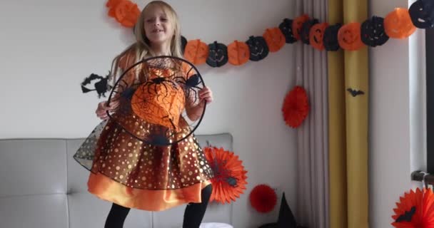 Niedliche kaukasische Mädchen mit blonden Haaren sieben Jahre alt in Hexenkleid und Hut Spaß haben und feiern Halloween zu Hause während Coronavirus covid-19 Pandemie und Quarantäne. Zeitlupe — Stockvideo