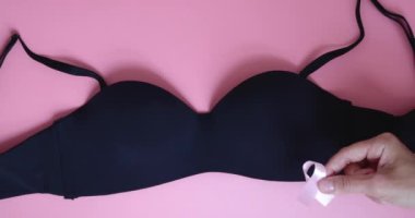 Pembe göğüs kanseri farkındalığı kurdelesi, siyah iç çamaşırı ve pembe arka planda eller. Yavaş çekim.