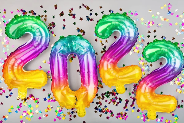Szczęśliwego Nowego Roku 2022 tle. Metalowe balony tęczowe kolory na szarości z konfetti. Płaskie ułożenie, widok z góry, makieta, nad głową. Święto zimowe — Zdjęcie stockowe